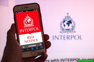 Czerwona nota Interpolu na wyświetlaczu telefonu. W tle logo Interpolu. Czerwona nota Interpolu na wyświetlaczu telefonu. W tle logo Interpolu.