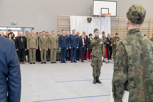 Kadet prezentuje broń, z tyłu stoją goście. Kadet prezentuje broń, z tyłu stoją goście.