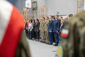 Zaproszeni goście oraz rodzice stoją w hali sportowej. Zaproszeni goście oraz rodzice stoją w hali sportowej.