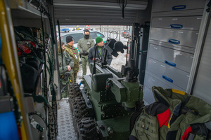 Widok z wnętrza pojazdu pirotechnicznego. Na pierwszym planie stoi robot, na drugim planie Wojewoda mazowiecki, płk SG Dariusz Lutyńśki oraz funkcjonariusze Zespołu Interwencji Specjalnych. Widok z wnętrza pojazdu pirotechnicznego. Na pierwszym planie stoi robot, na drugim planie Wojewoda mazowiecki, płk SG Dariusz Lutyńśki oraz funkcjonariusze Zespołu Interwencji Specjalnych.