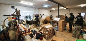 Funkcjonariusze stoją w pomieszczeniu gdzie produkowano nielegalny towar. Na podłodze leży zatrzymany. Funkcjonariusze stoją w pomieszczeniu gdzie produkowano nielegalny towar. Na podłodze leży zatrzymany.