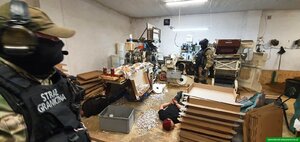 Funkcjonariusze stoją w pomieszczeniu gdzie produkowano nielegalny towar. Na podłodze leży zatrzymany. Funkcjonariusze stoją w pomieszczeniu gdzie produkowano nielegalny towar. Na podłodze leży zatrzymany.