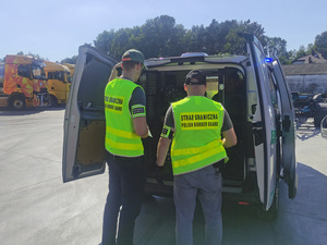Funkcjonariusze stoją przed samochodem, cudzoziemcy zapinają pasy bezpieczeństwa. Funkcjonariusze stoją przed samochodem, cudzoziemcy zapinają pasy bezpieczeństwa.