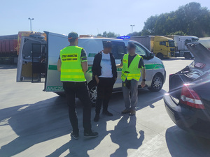 Funkcjonariusze i cudzoziemiec stoją przed samochodem służbowym. Funkcjonariusze i cudzoziemiec stoją przed samochodem służbowym.