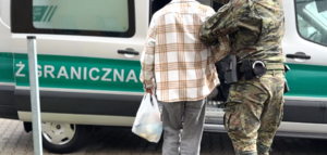 Funkcjonariusz prowadzi do samochodu cudzoziemca. Funkcjonariusz prowadzi do samochodu cudzoziemca.