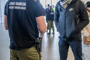 Funkcjonariusz i cudzoziemiec stoją w hali terminala. Funkcjonariusz i cudzoziemiec stoją w hali terminala.