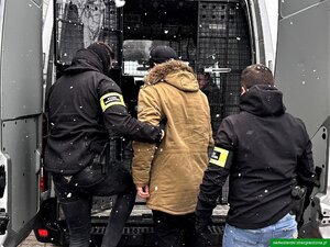 Funkcjonariusze wprowadzają cudzoziemca do pojazdu służbowego. Funkcjonariusze wprowadzają cudzoziemca do pojazdu służbowego.