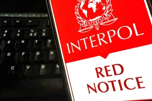 Czerwona Nota Interpolu wyświetlona na telefonie trzymanym w ręku. W tle klawiatura. Czerwona Nota Interpolu wyświetlona na telefonie trzymanym w ręku. W tle klawiatura.