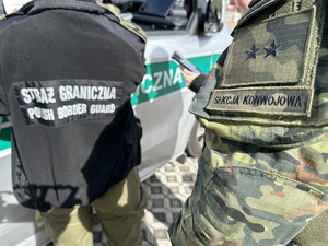 Funkcjonariusze stoją przy samochodzie służbowym. Funkcjonariusze stoją przy samochodzie służbowym.