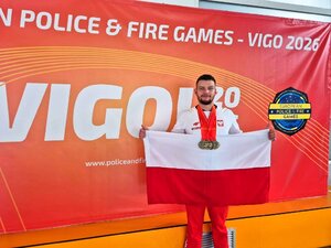 Funkcjonariusz stoi z flagą Polski, na szyi zawieszone ma medale. Funkcjonariusz stoi z flagą Polski, na szyi zawieszone ma medale.
